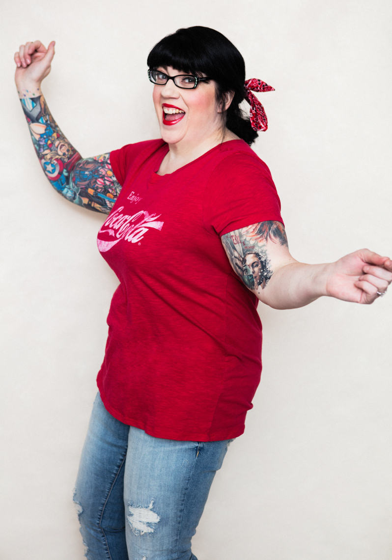 A beauty portrait of a middle age beautiful women, showcasing her natural beauty, femininity and style.  She wears distressed jeans and red coca-cola T shirt. She has a tattoo sleeves.  This portrait was created by Steve Glass, owner of the Portrait Studio of Glass Photography. They offer a beauty portrait service (a makeover portrait) session, where professional hair, professional makeup, professional styling are provided in the sitting fee. In all of his portraits he is looking to uncover the unique interests, creativity and beauty that each person possesses. This deepest portion of a person that is created in the image of God, the Imago Dei. Steve Glass, a professional portrait photographer of Glass Photography services the men, women, children, kids, families, business and people of Fort Collins, Windsor, Loveland, Wellington and the surrounding areas of Northern Colorado and southern Wyoming (and sometime Denver), through professional photography by creating timeless portraits and heirloom prints, ranging from corporate portraits, corporate headshots, environmental portraits, editorial portraits, and beauty portraits.
