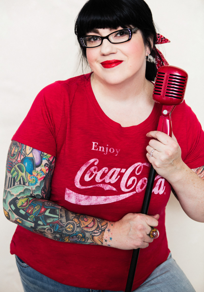 A beauty portrait of a middle age beautiful women, showcasing her natural beauty, femininity and style.  She wears distressed jeans and red coca-cola T shirt. She has a tattoo sleeves.  This portrait was created by Steve Glass, owner of the Portrait Studio of Glass Photography. They offer a beauty portrait service (a makeover portrait) session, where professional hair, professional makeup, professional styling are provided in the sitting fee. In all of his portraits he is looking to uncover the unique interests, creativity and beauty that each person possesses. This deepest portion of a person that is created in the image of God, the Imago Dei. Steve Glass, a professional portrait photographer of Glass Photography services the men, women, children, kids, families, business and people of Fort Collins, Windsor, Loveland, Wellington and the surrounding areas of Northern Colorado and southern Wyoming (and sometime Denver), through professional photography by creating timeless portraits and heirloom prints, ranging from corporate portraits, corporate headshots, environmental portraits, editorial portraits, and beauty portraits.