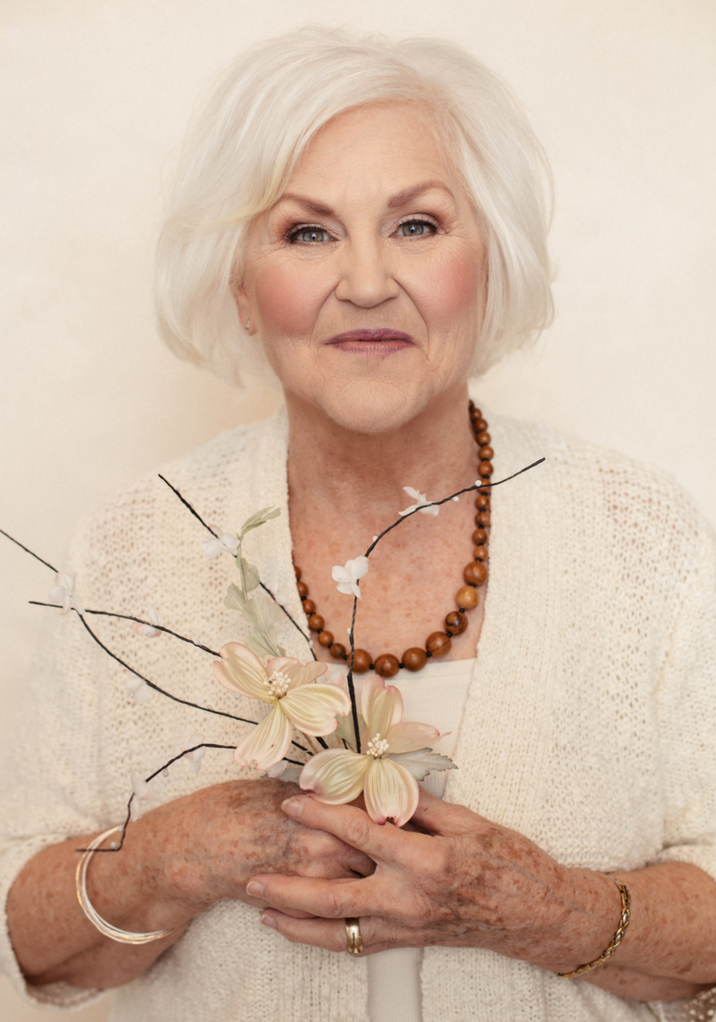 A beauty portrait of Kathryn Glass Addleman, a 75 year old, beautiful woman. This portrait was created by portrait photographer Steve Glass in his portrait studio Glass Photography through their beauty portrait service (a makeover portrait) session, where professional hair, professional makeup, professional styling are provided in the sitting fee. Kathy is wearing a bone sweater and blouse, holding a single flower. The portrait reveals her beauty, her femininity, her soul, her softness, her gorgeous. Steve Glass, is a professional portrait photographer of Glass Photography where he services the men, women, children, kids, families, business and people of Fort Collins, Windsor, Loveland, Wellington and the surrounding areas of Northern Colorado and southern Wyoming (and sometime Denver), through professional photography by creating timeless portraits and heirloom prints, ranging from corporate portraits, corporate headshots, environmental portraits, editorial portraits, and beauty portraits.
